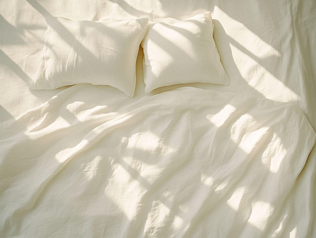 Soft white bedding with two pillows and dappled sunlight, illustrating that comfort goes beyond thread count. | Escapology Home