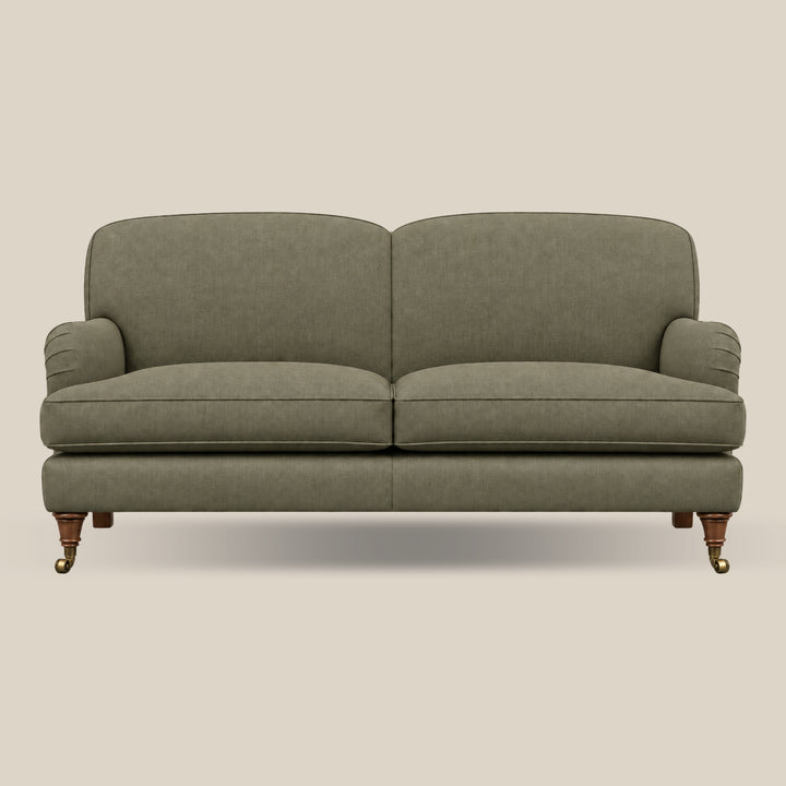 An upholstered Howard style sofa with two seat cushions and rounded arms, shown from the front against a plain warm beige background. The fabric is a muted sage green, and the legs are dark wood with brass casters.
