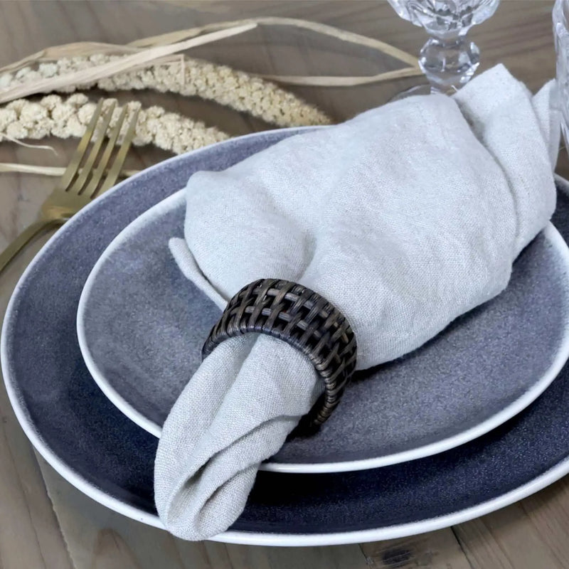 Stack of blue plates with a grey linen napkin and black wooden napkin ring on a wooden table.