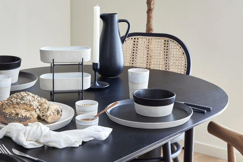 Dining table set with black and white dishes, bread, and a candle.